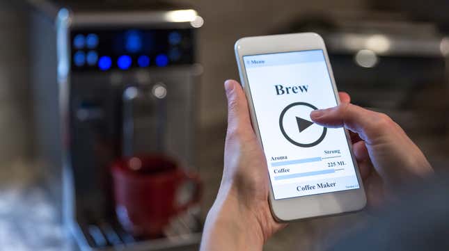 Hands holding smartphone connected to a smart coffeemaker, visible in background