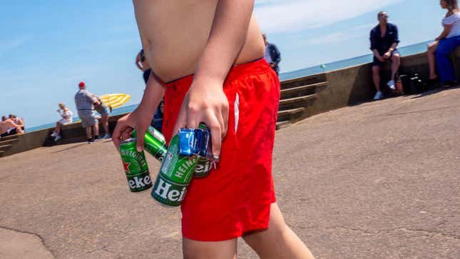 Man in swim trunks carries empty beer cans