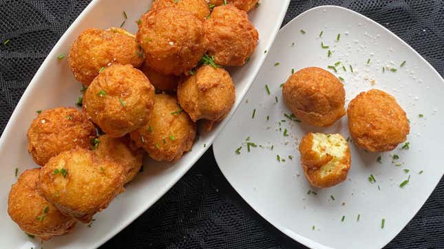 White bowl of fried potato puffs beside plate with three potato puffs served on it