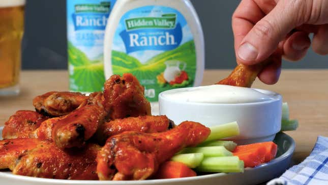Hand dips buffalo chicken wing into bowl of ranch dressing