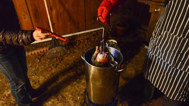 Two chefs dip a turkey into an outdoor fryer