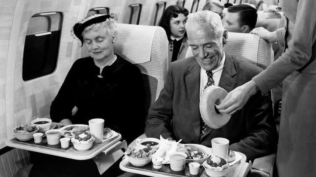 Black and white photo of man and woman receiving elaborate meal on plane