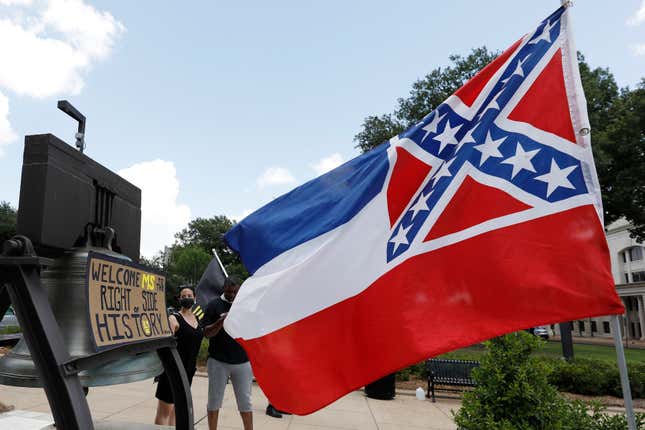 A Mississippi state flag waves adjacent to a flag change supporter’s sign that welcomes the state to “the right side of history,” outside the Capitol in Jackson, Miss., Sunday, June 28, 2020.