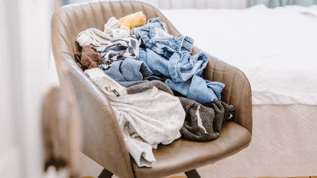 A pile of unfolded clothes on a tan leather chair.