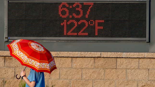 A pedestrian uses an umbrella to get some relief from the sun as she walks past a sign displaying the temperature on June 20, 2017 in Phoenix.