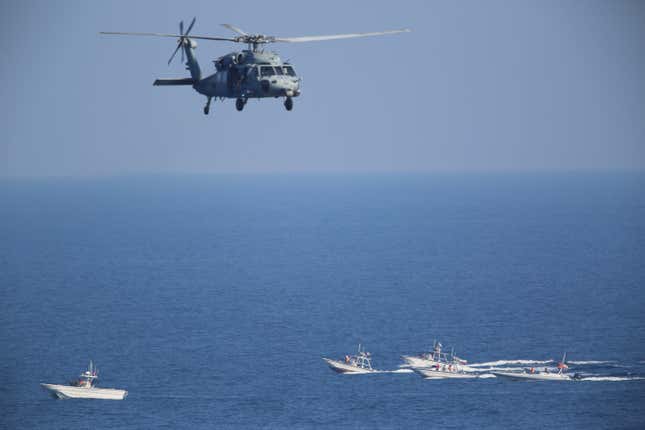 A U.S. Navy MH-60 Seahawk helicopter flies near Iranian Revolutionary Guards Corps Navy patrol boats. Note machine guns and other support weapons mounted on the bow. 2018.