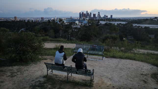 People sit on a hill overlooking Dodger Stadium and downtown Los Angeles on March 26, 2020.
