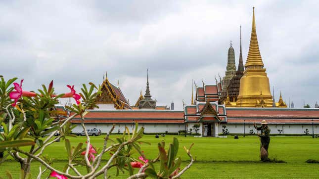 A cleaner sweeps a field in front of the Grand Palace in Bangkok.