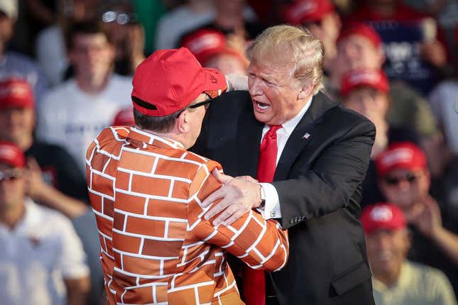 President Donald Trump calls up Blake Marnell, wearing a jacket with bricks representing a border wall, to the stage during a ‘Make America Great Again’ campaign rally.
