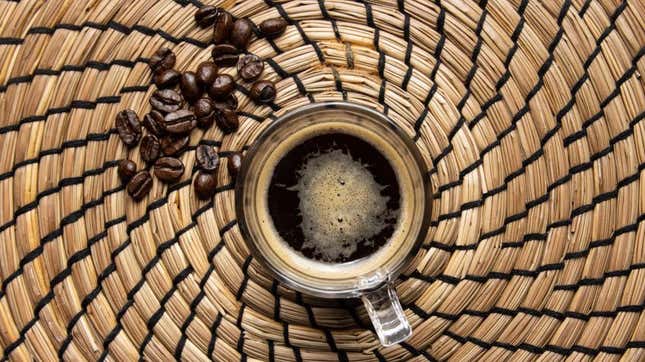Raw organic Arabica variety coffee beans and a coffee mug of glass on a straw background
