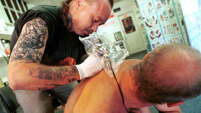 Tattoo artist leaning over to tattoo man's back