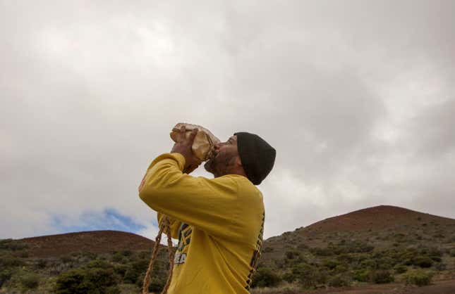 A Hawaiian who opposes construction of the Thirty Meter Telescope blows a conch shell near the summit of Mauna Kea in August, 2015. Image: Caleb Jones/AP