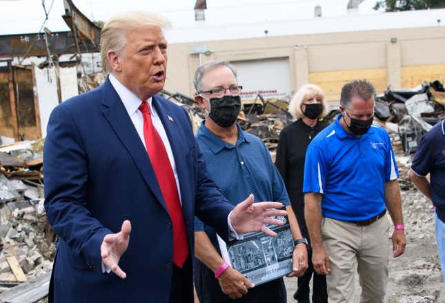 President Donald Trump speaks to the press as he tours an area affected by civil unrest in Kenosha, Wisconsin on September 1, 2020, as John Rode, center, the former owner of the building that contained Rode’s Camera Shop looks on holding a sign.