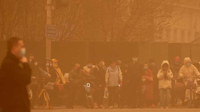 People wait to cross an intersection amid a sandstorm during the morning rush hour in Beijing, Monday, March 15, 2021.