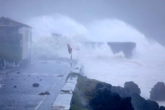 Waves crash on a seafront road in Horta.