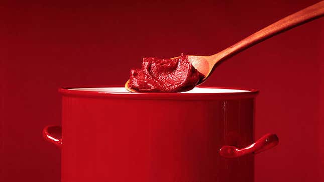 spoon of tomato paste hovering above a red cooking pot
