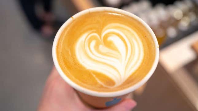 Hand holding latte with heart-shaped milk froth on top