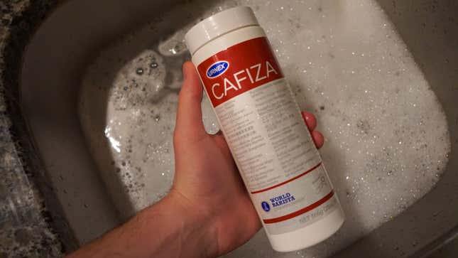 Bottle of Cafiza held over a sink full of hot water