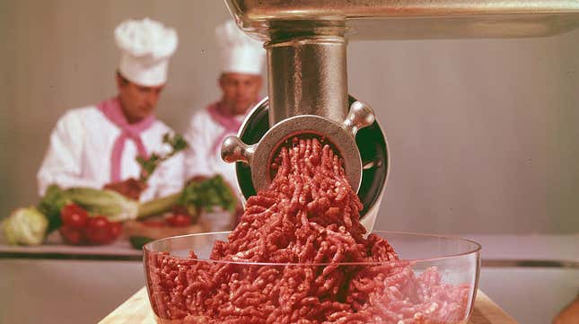 Close-up of ground beef in a glass bowl with chefs in background