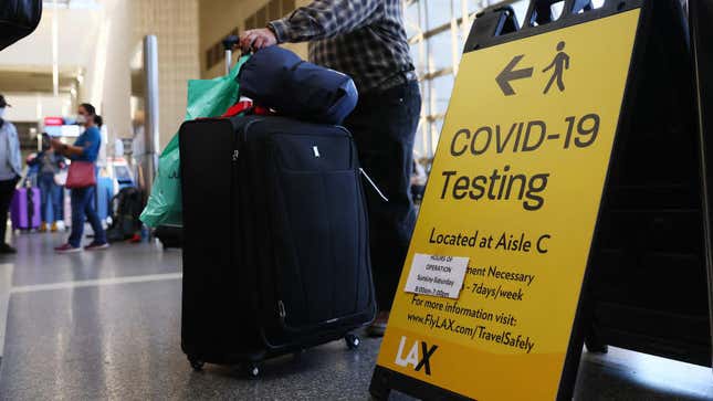 People wait in line to check in near a sign pointing to a COVID-19 testing area in the Tom Bradley International Terminal at Los Angeles International Airport (LAX) amid a COVID-19 surge in Southern California on December 22, 2020 in Los Angeles, California. 