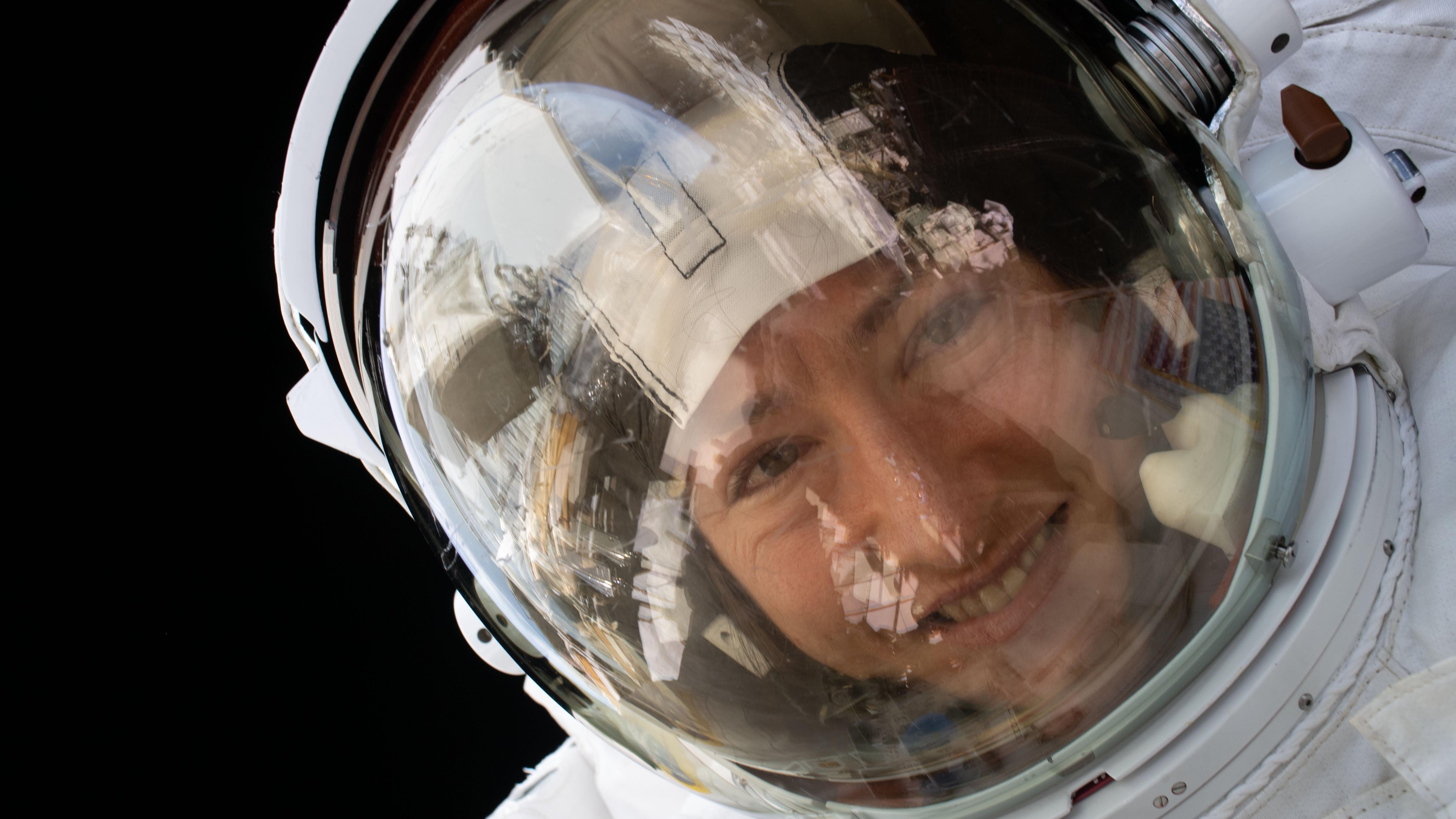 صورة رائدة فضاء ناسا كريستينا كوخ أثناء سيرها في الفضاء.  يمكن رؤية الأرض في انعكاس خوذتها.