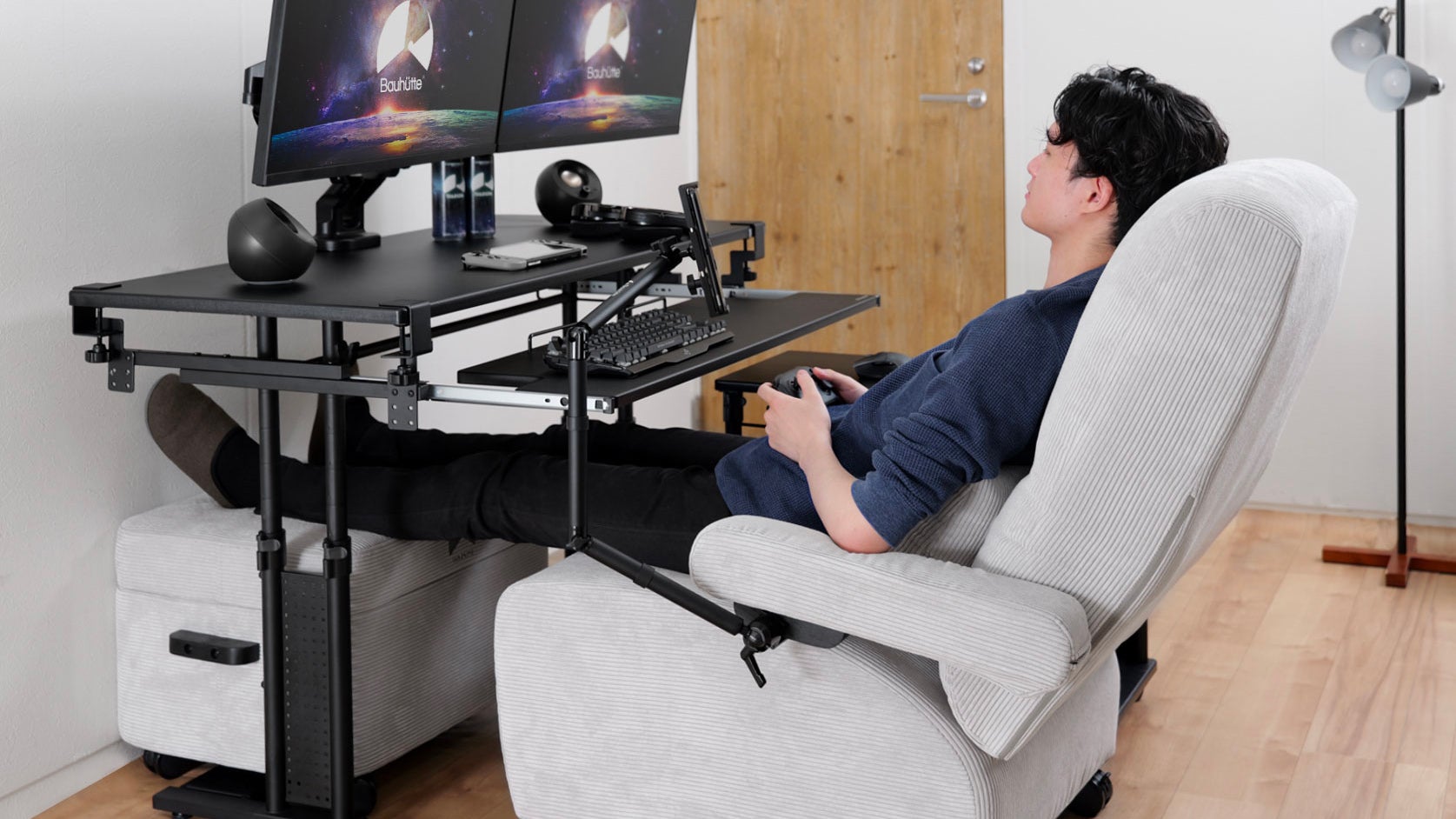 تم سحب لاعب يجلس في Bauhutte Gaming Sofa Deluxe إلى مكتب مع زوج من شاشات الكمبيوتر بزاوية لأسفل لمواجهتها.