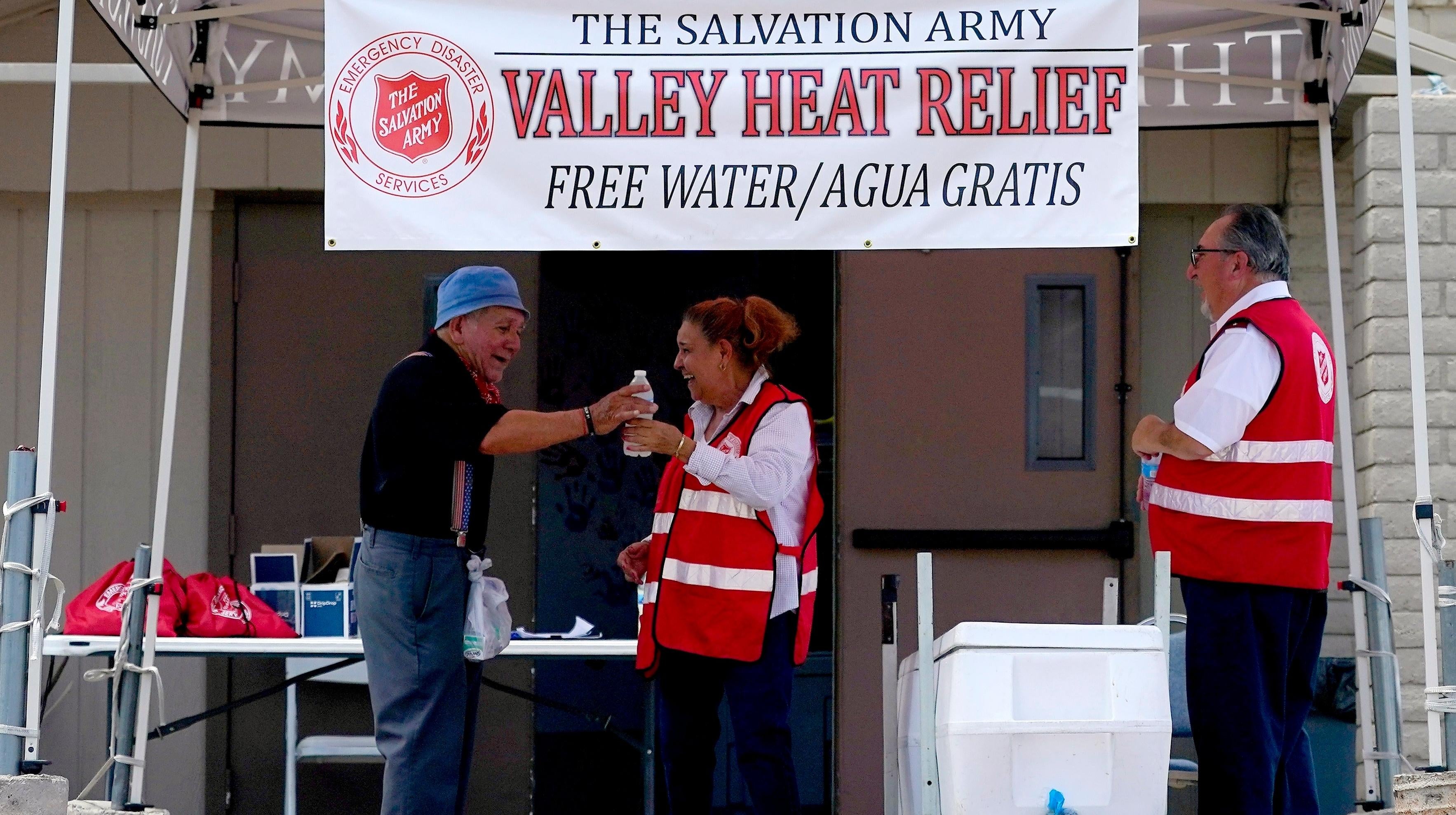 المتطوع في جيش الإنقاذ فرانسيسكا كورال ، في الوسط ، يعطي الماء لرجل في محطة فالي هيت ريليف الخاصة بهم ، في 11 يوليو 2023 في فينيكس.