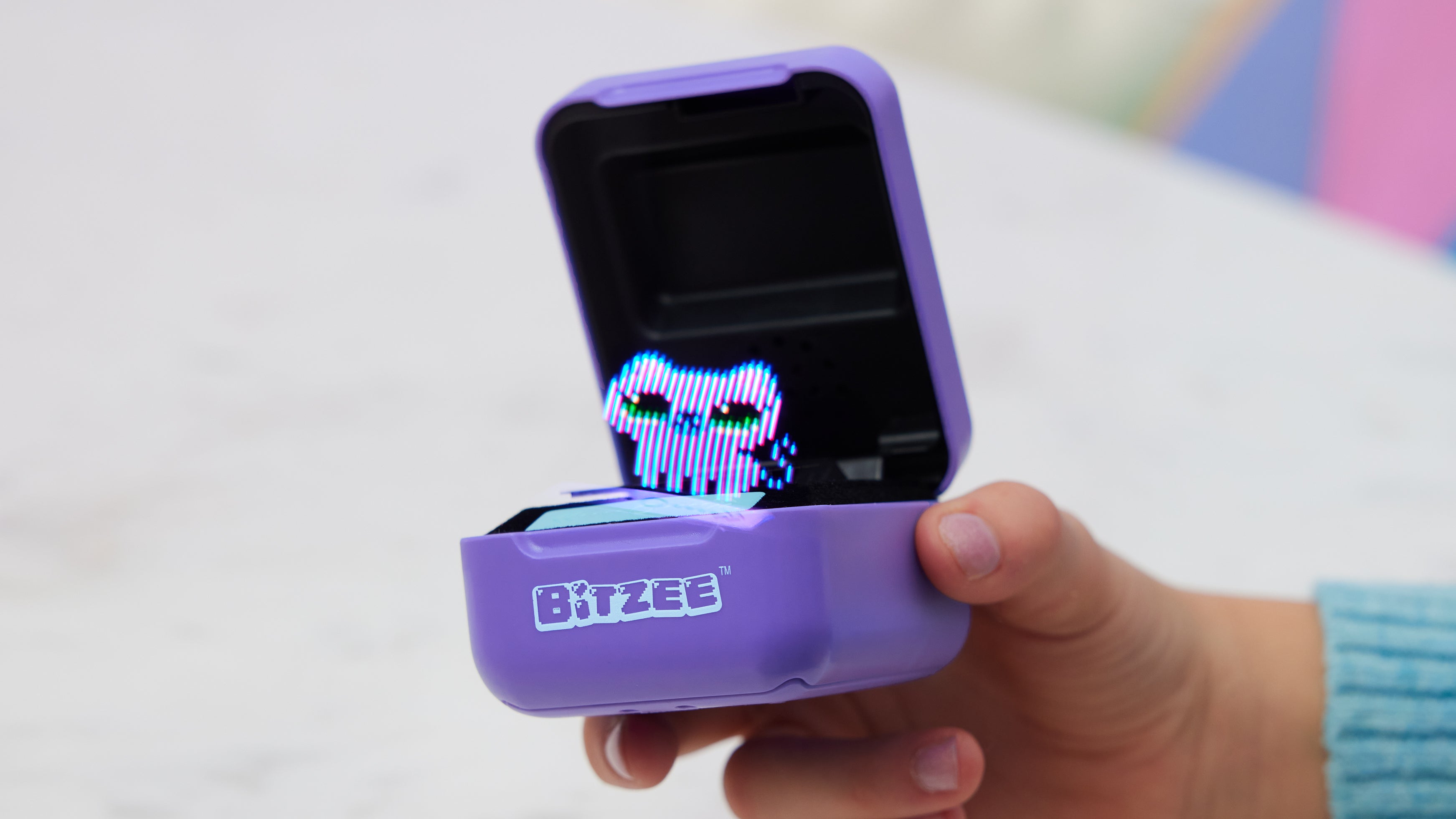 مستخدم يحمل حيوانًا أليفًا رقميًا من Bitzee وغطاءه مفتوحًا وقطة أرجوانية على الشاشة.