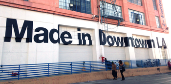 Two people walk past the American apparel factory building and outlet store in Los Angeles, California July 7, 2014. Ousted American Apparel Inc head Dov Charney supported workers in the clothing industry with his stance in favor of immigration rights and determination to keep jobs in the United States, but some employees are not returning the favor. Last month American Apparel&#039;s board dismissed Charney. It accused the chairman, president and chief executive of misusing corporate funds and failing to prevent the dissemination of nude photos of a female ex-employee who sued him. Picture taken July 7, 2014. To match Feature AMERICAN-APPAREL-WORKERS/ REUTERS/Lisa Baertlein (UNITED STATES - Tags: BUSINESS EMPLOYMENT SOCIETY CRIME LAW) - RTR3XO82