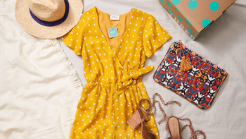 A yellow dress and accessories such as a bag and clothes lie flat on a bed
