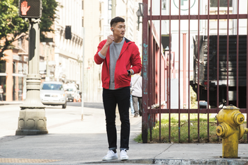 Asian man in street clothing wearing a red sweater in a city setting on the street. He&#039;s wearing flyer in nightfall blue and ionic in blue gray and silver gray.