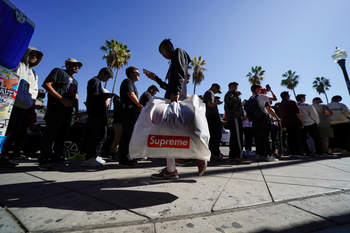 A shopper with a bag full of purchases walks past ticketed shoppers waiting on the sidewalk outside the Supreme clothing store on Fairfax in Los Angeles