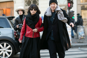PARIS, FRANCE - JANUARY 21: Rei Kawakubo, Comme des Garcons creative director, and Adrian Joffe, Dover Street Market and Comme des Garcons president, exit the Gosha Rubchinskiy show on January 21, 2016 in Paris, France. Rei wears a red Comme des Garcons leather jacket, black sunglasses, a black scard, and black dress. (Photo by Melodie Jeng/Getty Images)