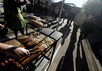A line of voters stands behind a grill covered with sausages and onions