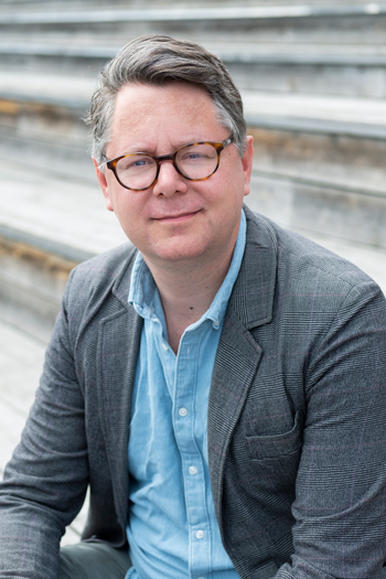 Photo of Financial Times journalist Robin Wigglesworth, sitting on steps and wearing a button-down shirt and grey jacket.