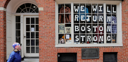 A pedestrian walks past a sign in a shop window reading "We Will Return Boston Strong"