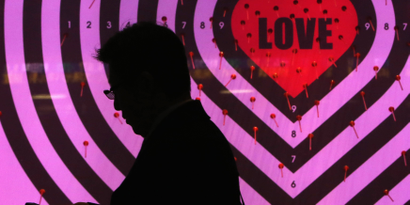 A man using his mobile phone walks past a shop window with signs advertising the upcoming Valentine's Day, at a luxury store in Tokyo