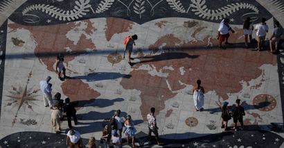 People take pictures at a square decorated with a giant world map in Lisbon