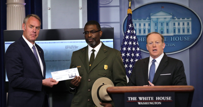 Interior secretary Ryan Zinke accepts Trump's check at a White House press conference.