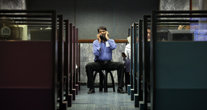 A man uses a phone between booths while monitoring share prices during a trading session at the Karachi Stock Exchange August 10, 2011.