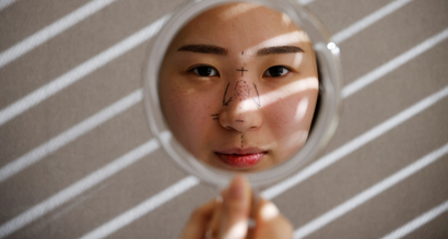Woman looking in mirror with markings on her nose pre-nose job