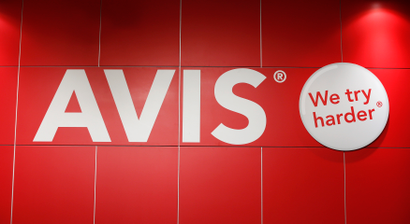 The Avis rental car company is pictured on a red wall with the phrase "We Try Harder."