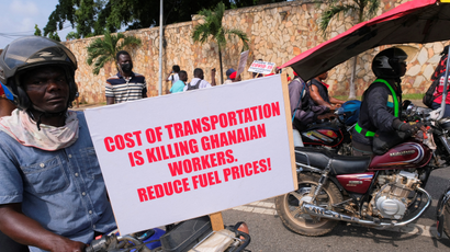 Men riding motorcycles hold placards protesting high costs of living in Ghana