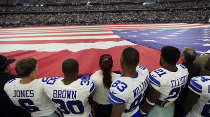 football players hold horizontal US flag during the National Anthem