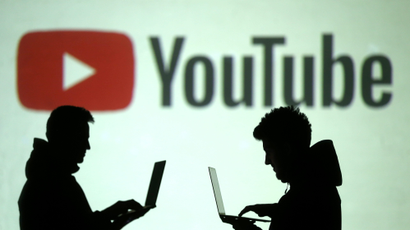 Silhouettes of mobile device users are seen next to a screen projection of Youtube logo in this picture
