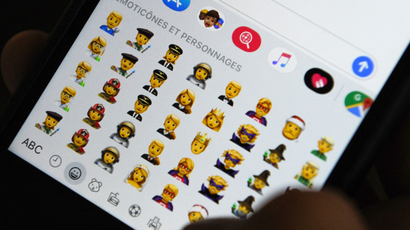A person holds an iPhone with the emoji keyboard displayed
