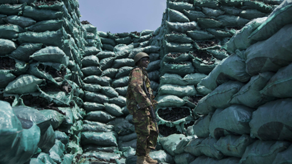 A Kenyan soldier stands amongst piles of charcoal in Somalia.