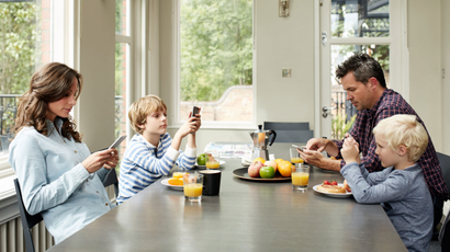 Shot of a family of four distracted by their cellphones while eating breakfast together