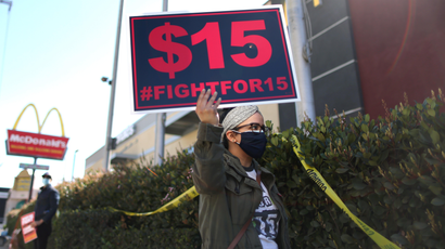 A person holding a Fight for $15 sign and protesting outside of a McDonald's