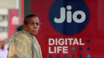 A woman waits at a bus stop with an advertisement of Reliance Industries' Jio telecoms unit in Mumbai